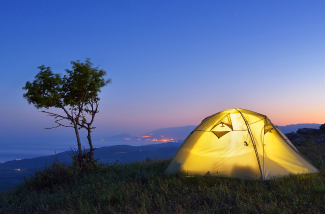 A tent with people camping at night.